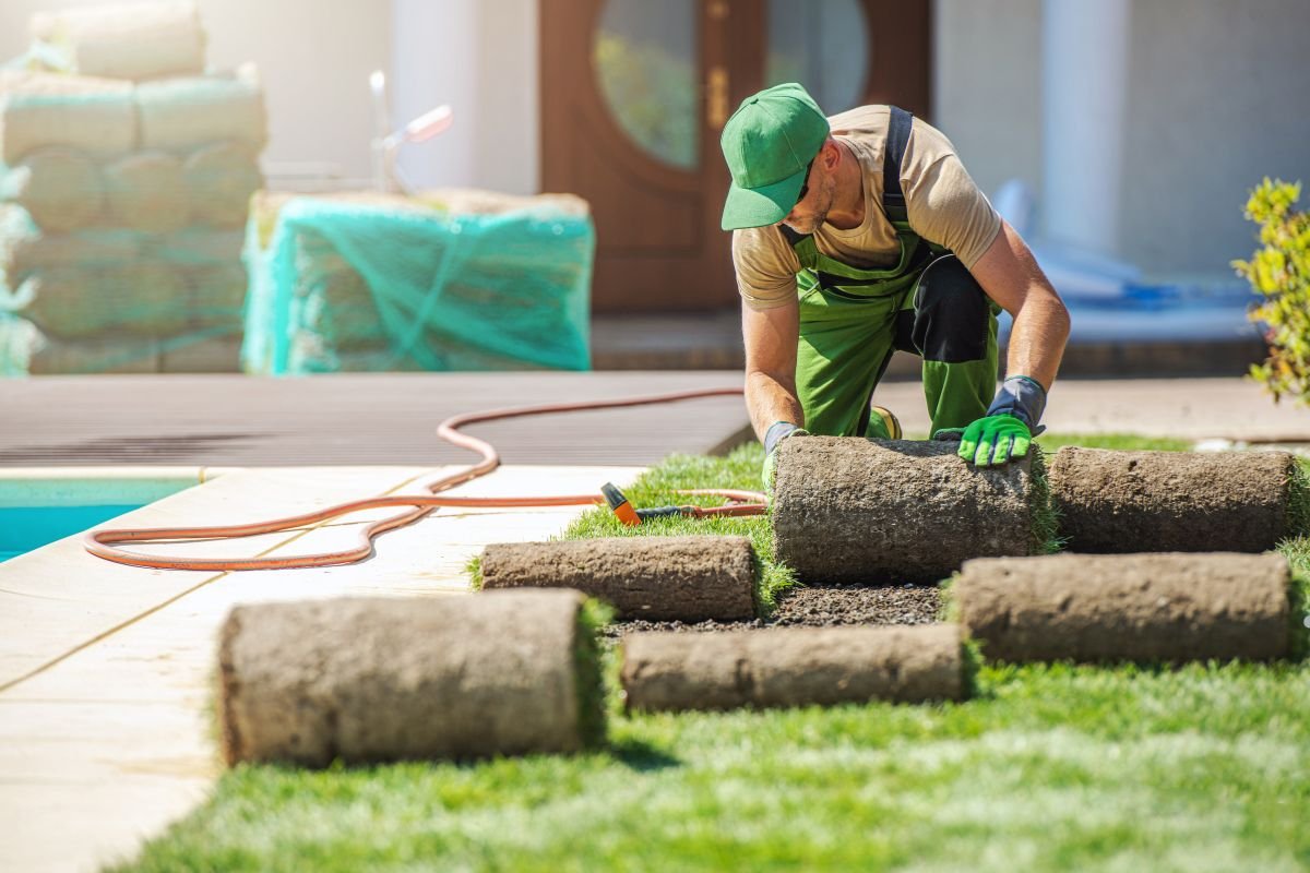 A man in green overalls performs lawn care, tending to a well-maintained grassy area.
