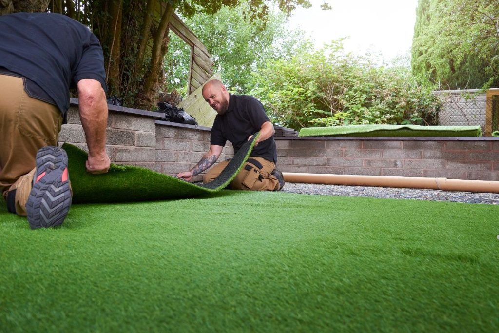 Two men installing artificial grass in a backyard as part of a professional lawn care service.