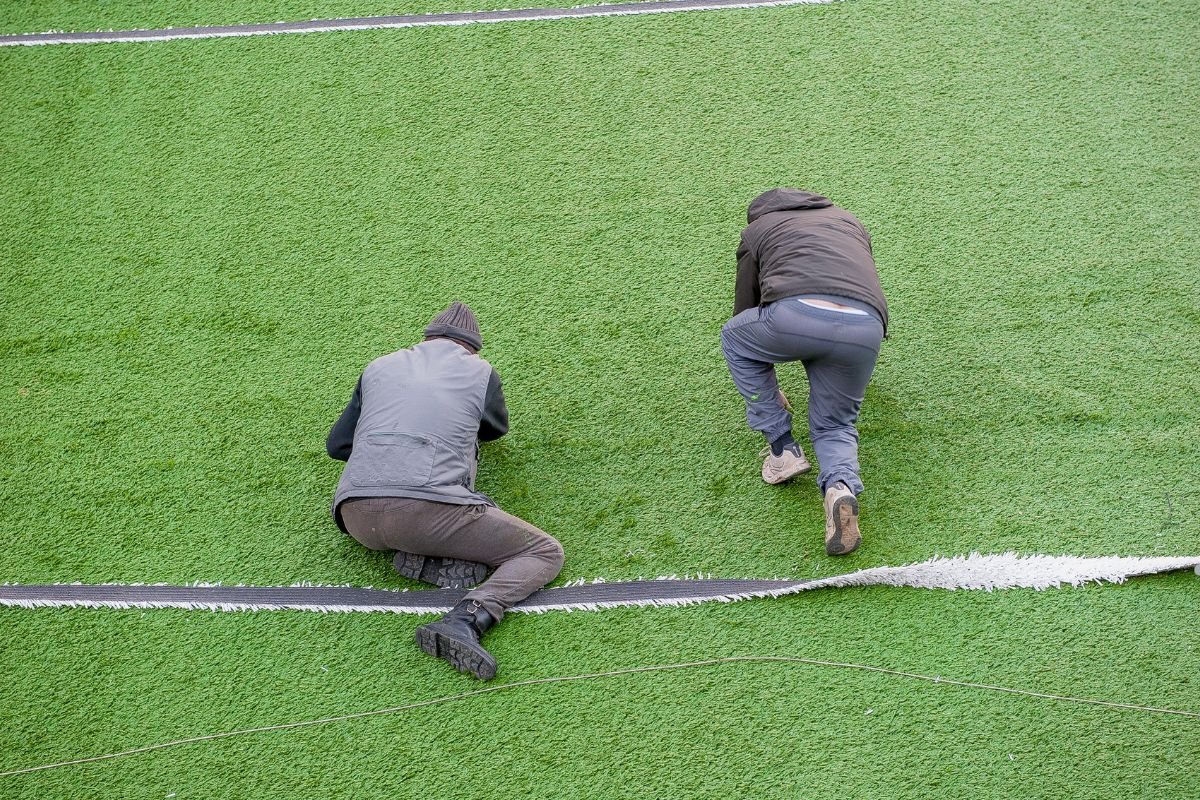 Two men performing lawn care on a soccer field, ensuring the grass is well-maintained for optimal play conditions.