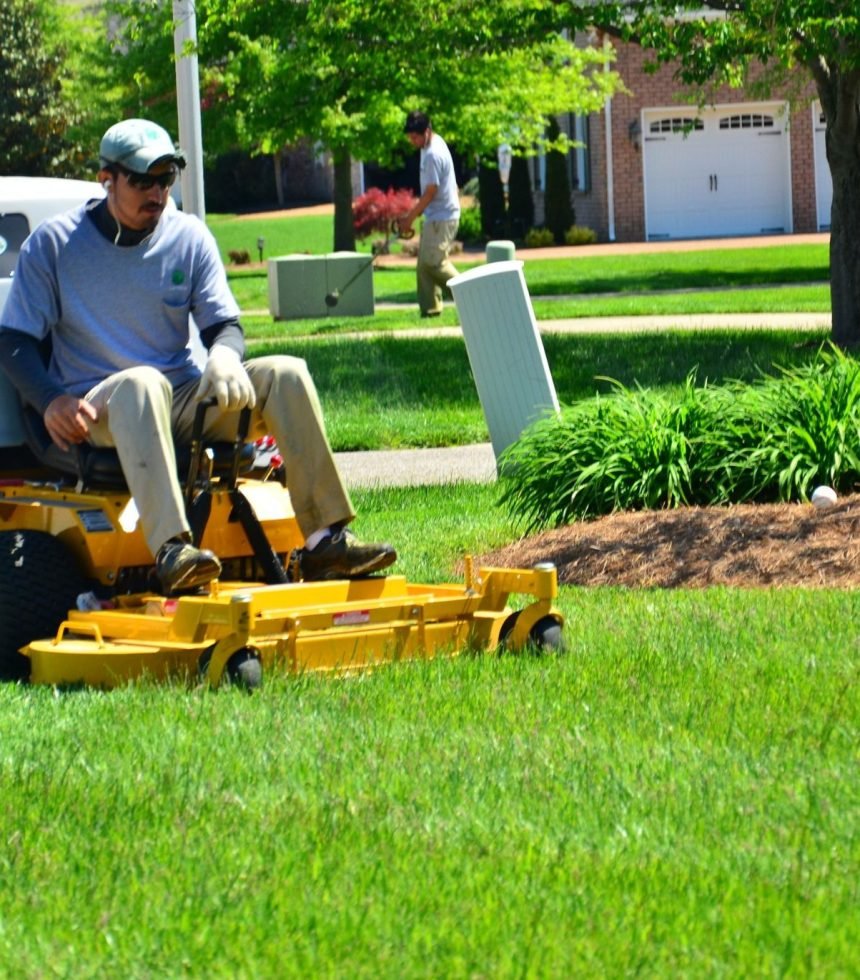 A man operating a lawn mower, trimming grass in a well-maintained yard.