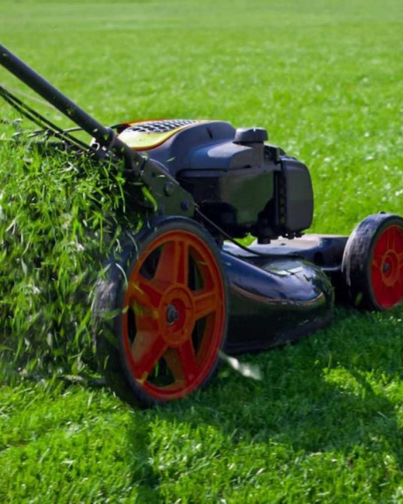 A lawn mower is actively cutting grass on a lush green field under clear skies.